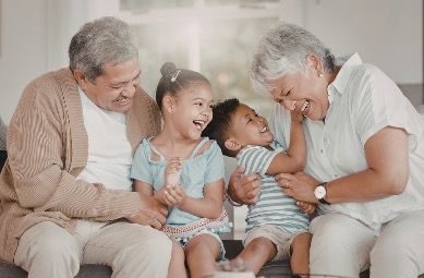 a grandfather, grandmother, and two grandchildren - a boy and a girl - smiling and sitting on the couch