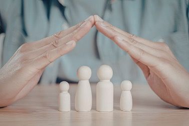 Hands forming a protective triangle above four small white figurines on a table.