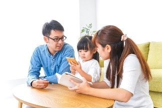 a mom, dad, and young daughter sit at a table looking at a book