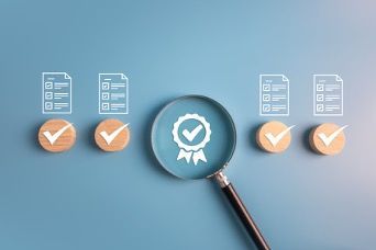 Magnifying glass over blue checkmark badge with document and approval icons on a blue background
