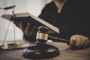 a judge at a desk holding a book, a gavel. Scales of justice on the desk