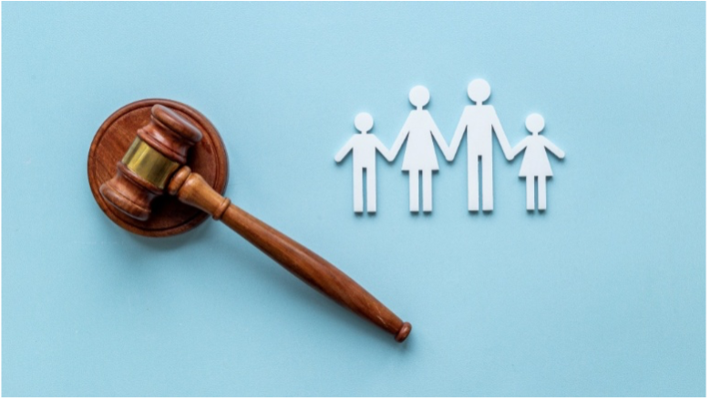 A wooden judge 's gavel is sitting next to a paper cut out of a family holding hands.