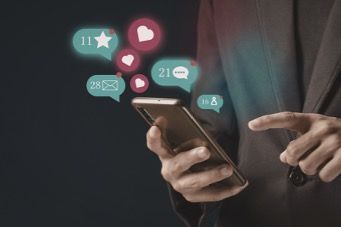 Person using a smartphone with floating social media notification icons and heart likes.