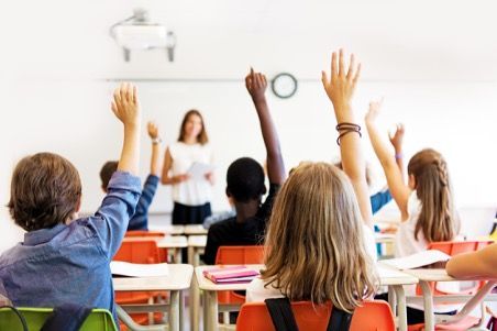 A group of children are raising their hands in a classroom.