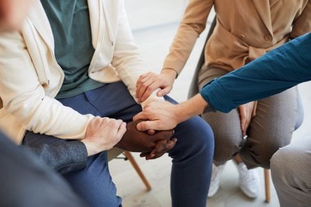 Group of people sitting in a circle, holding hands, in a room.
