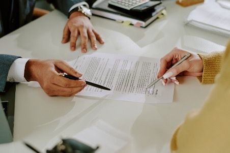 Two people reviewing a document, one pointing, the other about to sign it. Office setting.