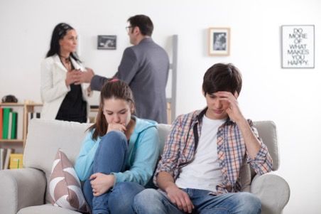 Teenagers on a couch looking sad, parents arguing in the background. Interior setting, neutral colors.