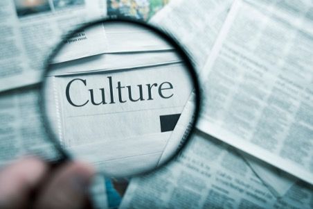 A person is holding a magnifying glass over a newspaper that says culture