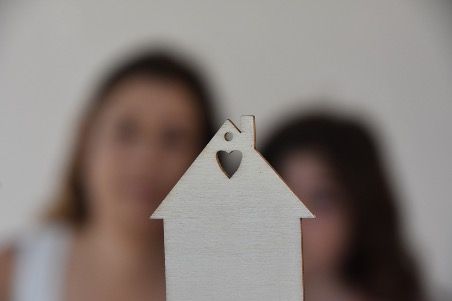 Wooden house cutout with heart, two blurred women in background.