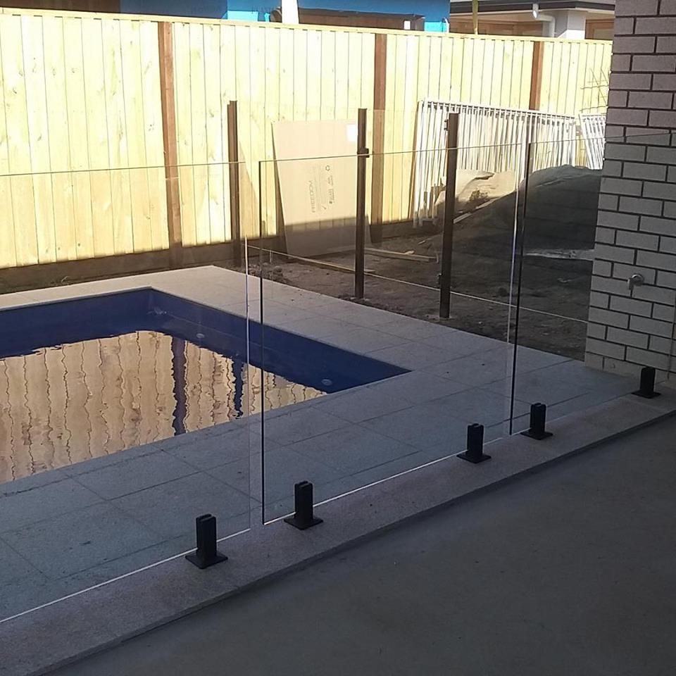 Backyard pool area with glass fence, blue water, and tan deck beside a brick wall