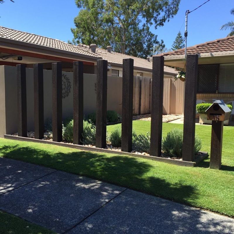 Backyard with a wooden fence, green lawn, and tiled patio beside a house in bright sunlight