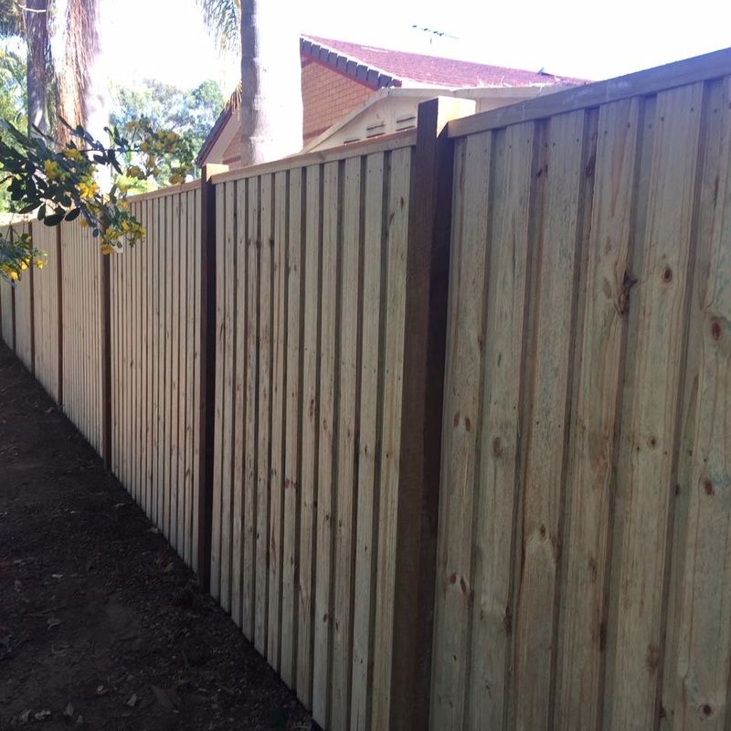 Wooden fence along a narrow side yard beside a house, with sunlight and trees overhead