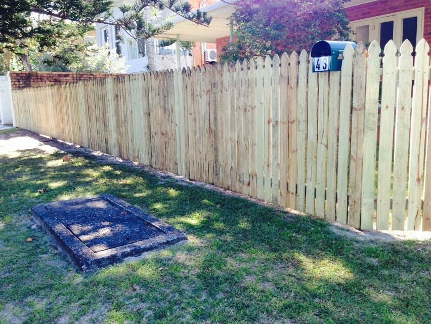 Backyard with a weathered wooden fence, grassy lawn, and a small raised cover near the left side.