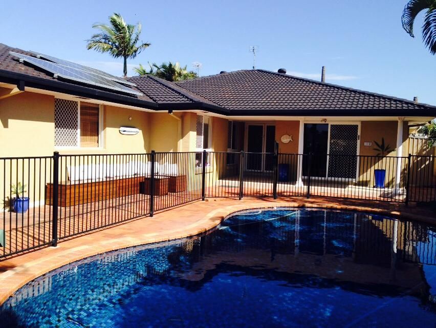 Backyard pool beside a single-story house with a fenced patio under a sunny blue sky