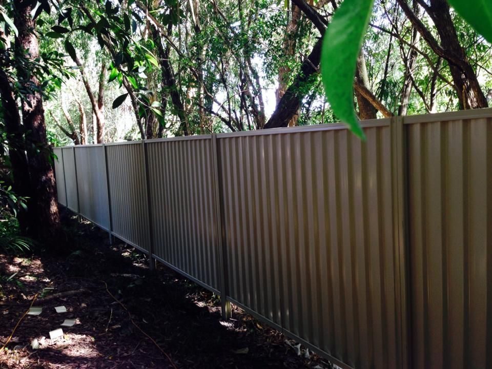 Long metal fence beside a wooded path with sunlight filtering through trees