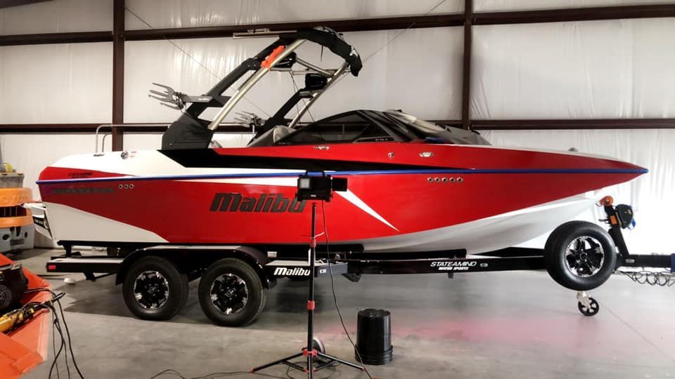Red and white Malibu boat on a trailer inside a building with its tower up.
