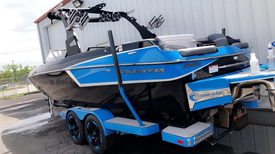 Blue and black wake boat on trailer; tower, steps, and logo visible.