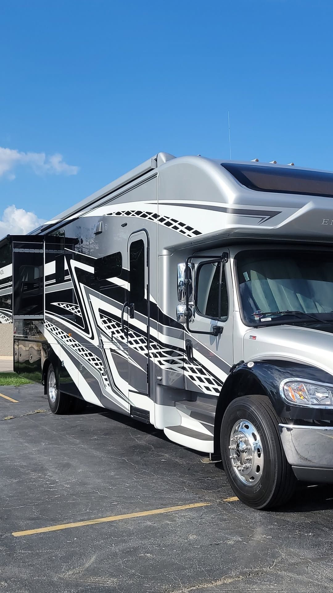 A rv is parked in a grassy field with a guitar , chairs and a surfboard.