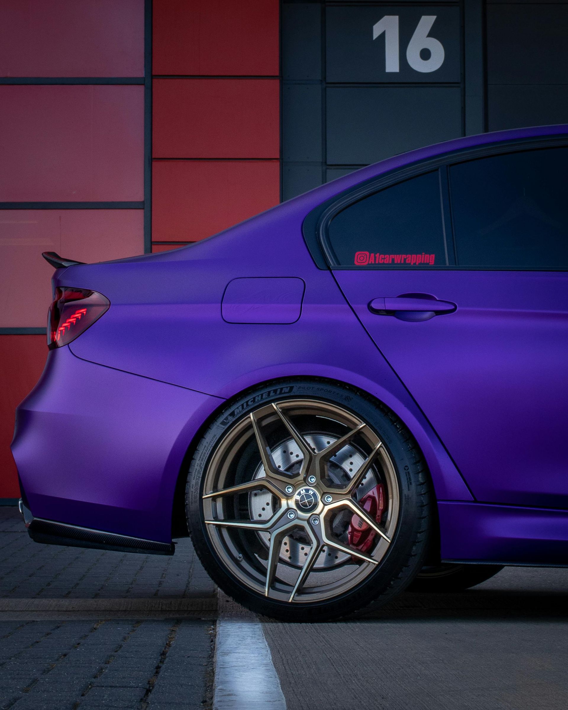 Purple sports car, custom wheels, parked in front of building with the number 16.