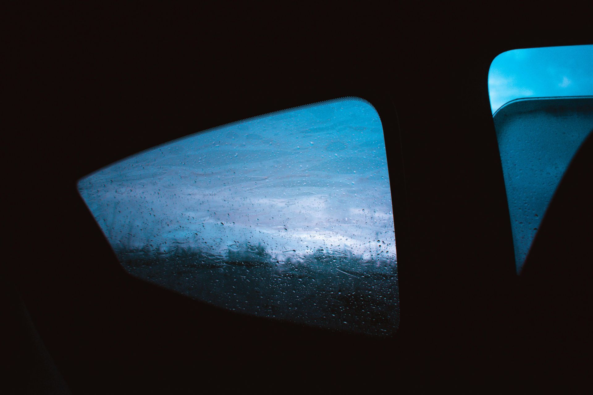 View of a stormy sky through rain-streaked car windows, interior is dark.