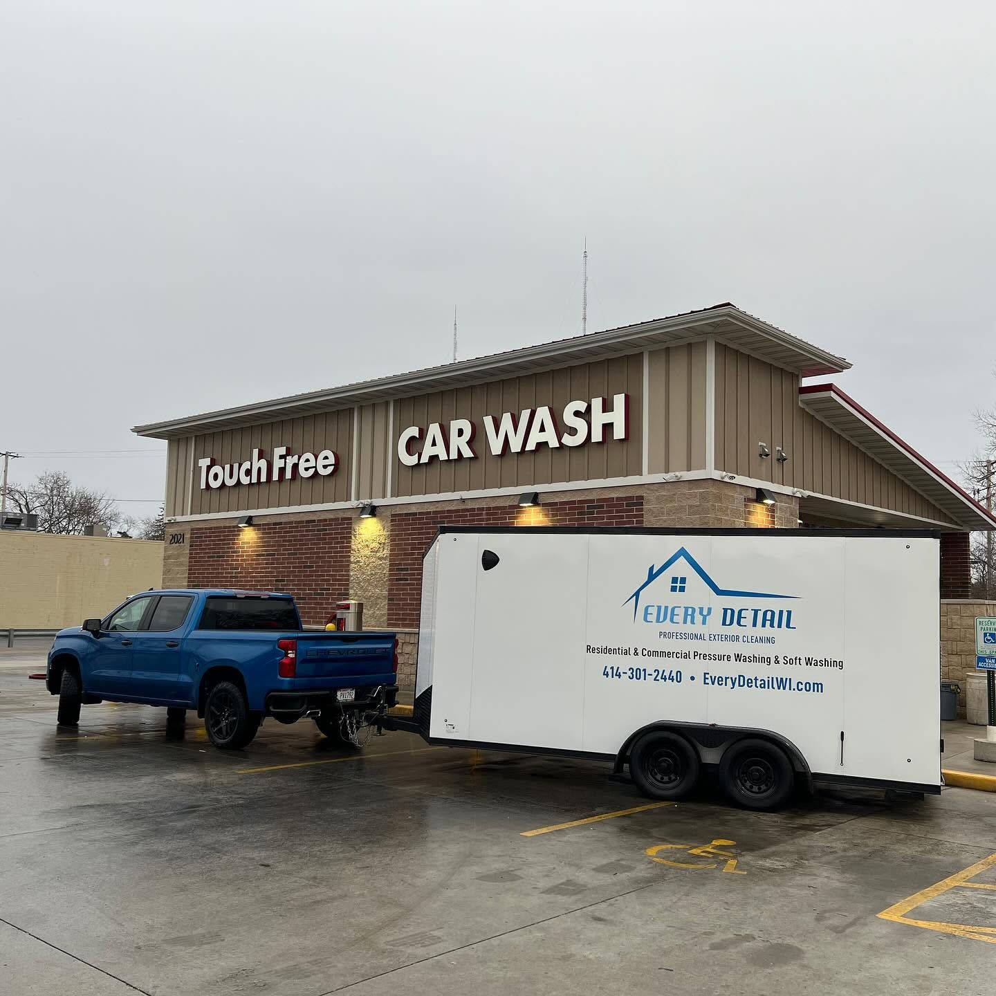 Blue pickup and white trailer parked outside a Touch-Free Car Wash on a rainy day