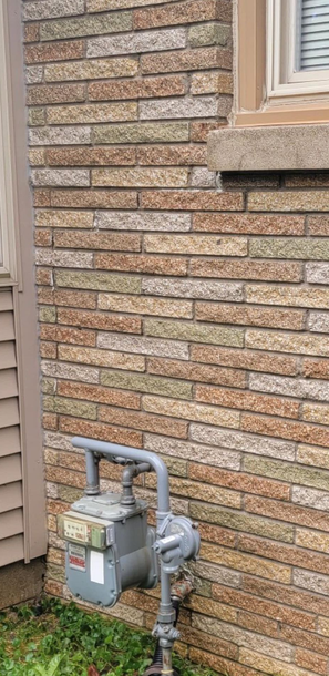 Gas meter and pipes mounted on a brick house wall beside a window and door.