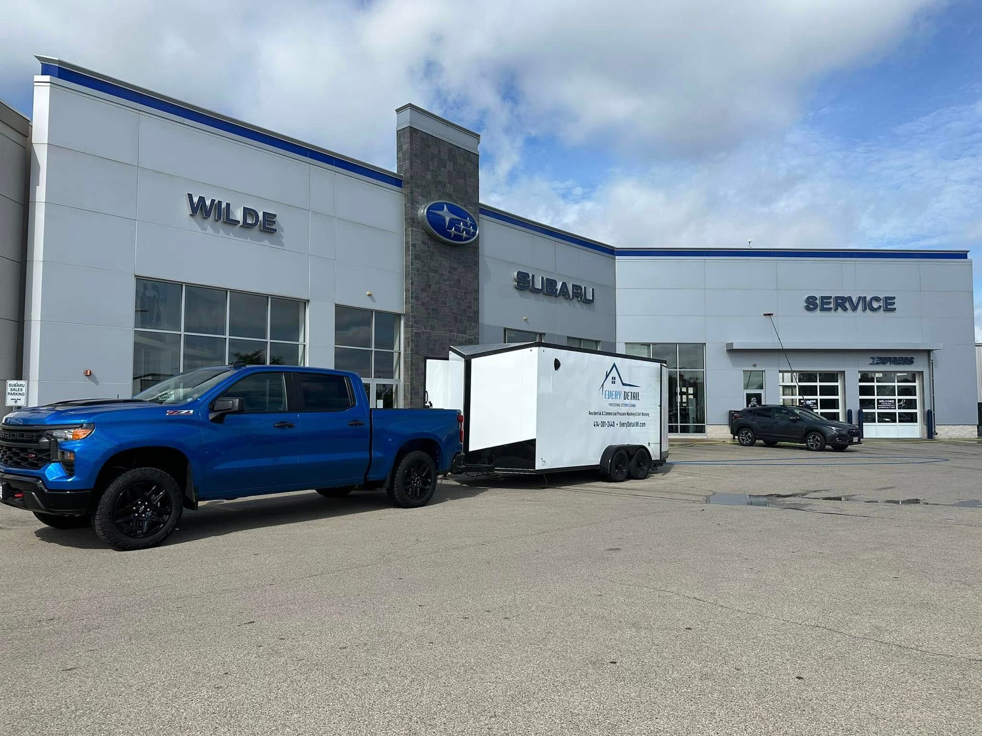 Blue pickup truck and white trailer parked outside a Ford dealership service center.