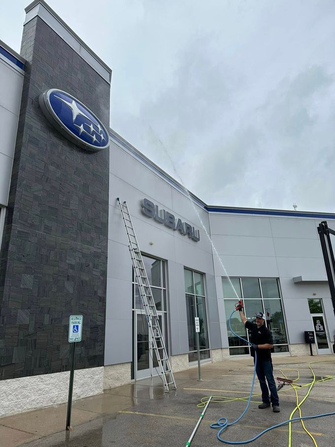 Entrance of a Subaru dealership on a cloudy day, with a worker standing outside near a pressure washer.