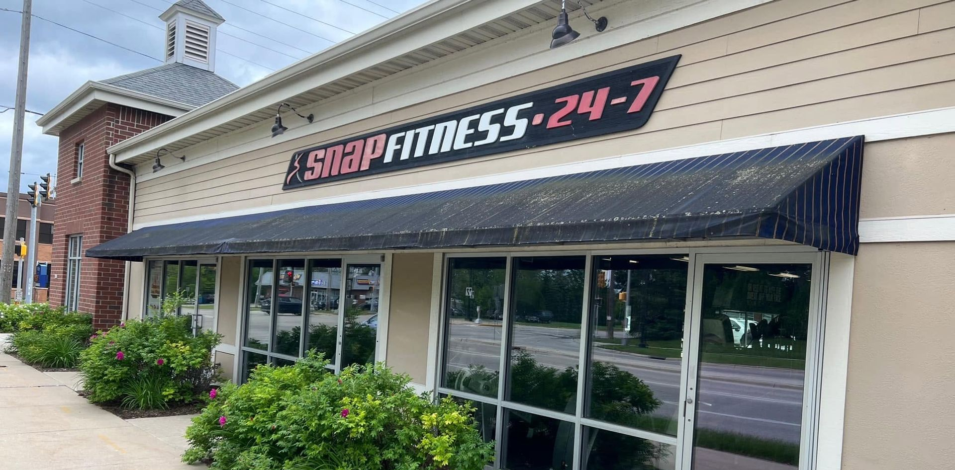 Fitness24-7 gym storefront with glass windows, black awning, and brick building exterior