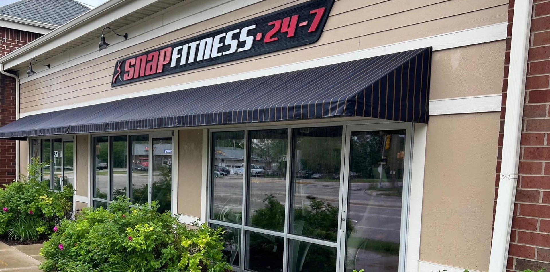 Storefront of Snap Fitness 24-7 with black awning and glass windows, exterior view in daylight