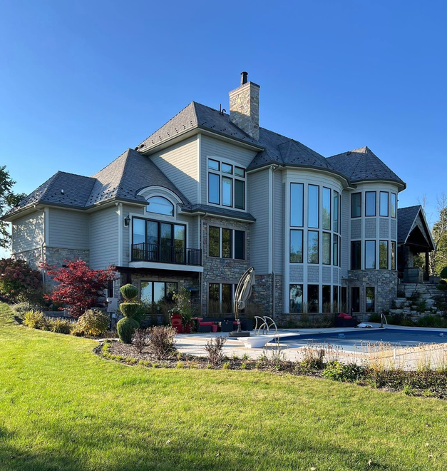 Large stone house with gray roof and tall windows, viewed across a green lawn under a clear blue sky