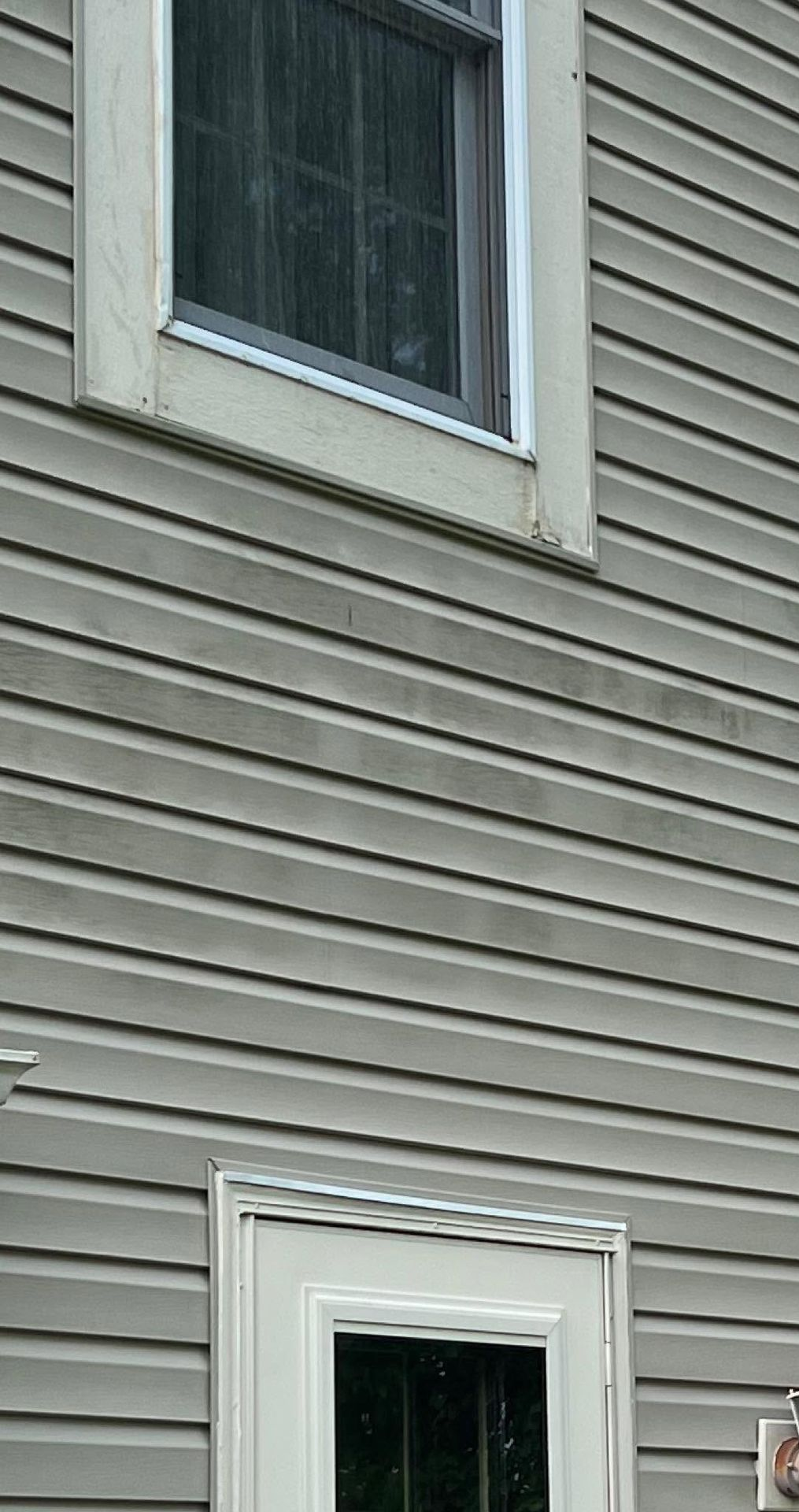 Gray house siding with two white-framed windows, one near the top and one near the bottom.