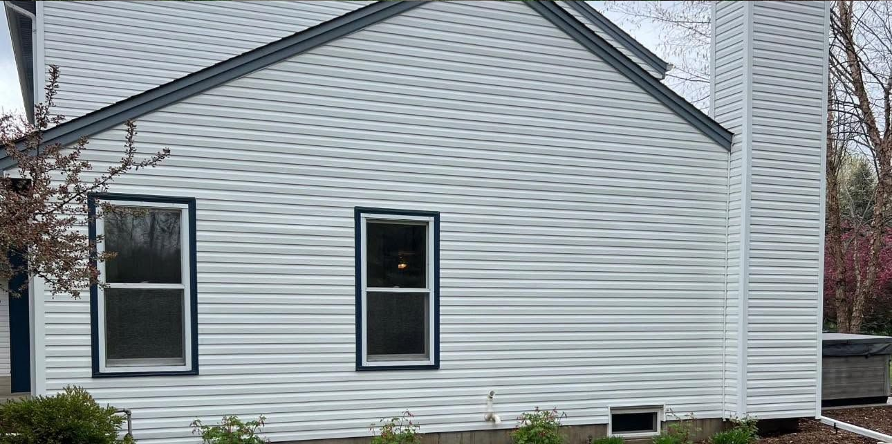 White house exterior with two windows and a side wall, showing a sloped roof and vinyl siding