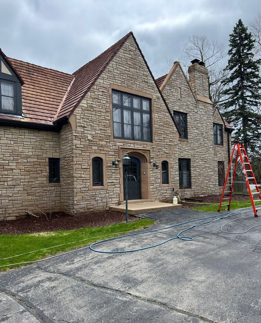 Stone house exterior with red roof and a ladder by the driveway on a cloudy day
