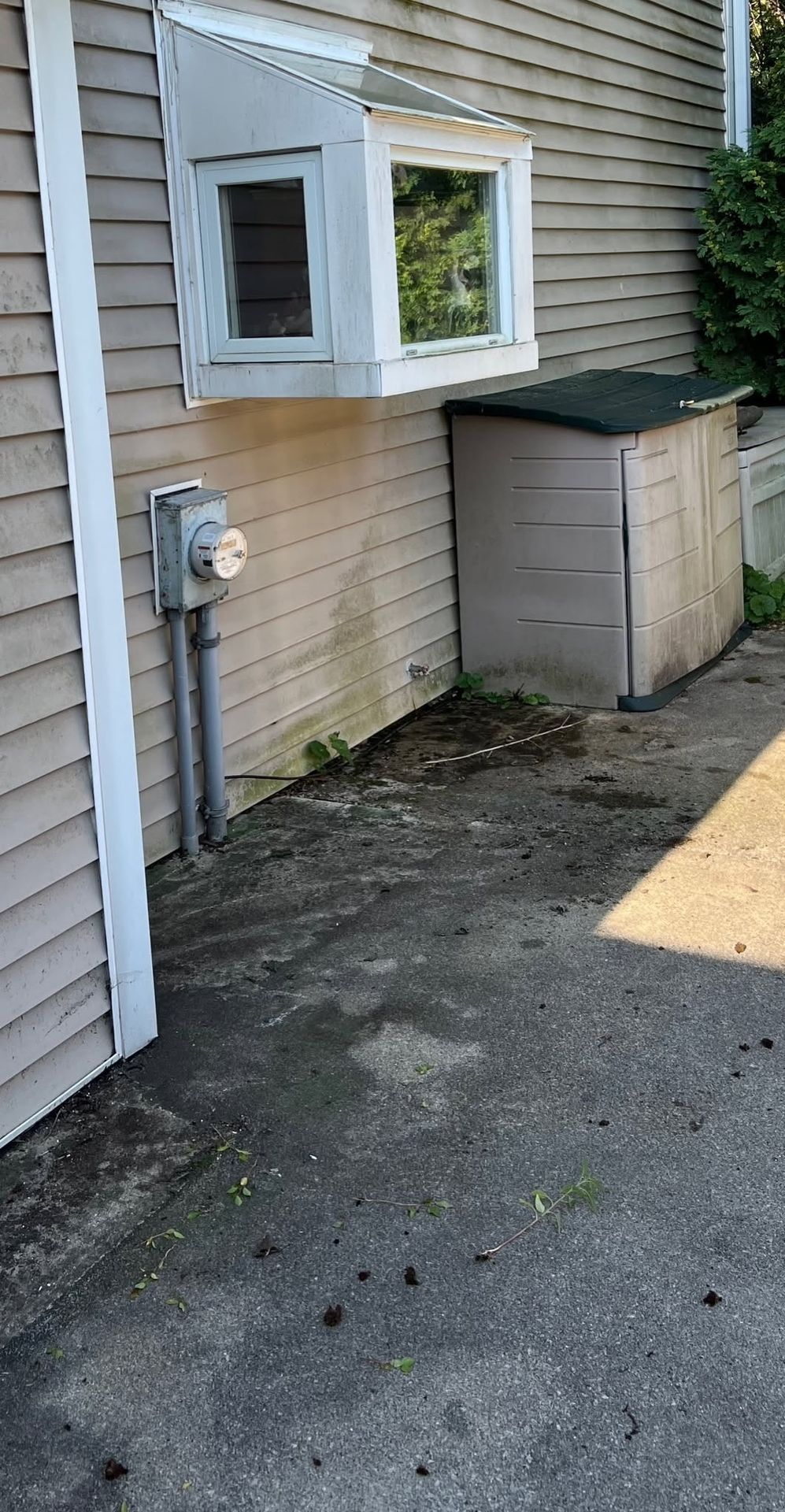 Side of a beige house with a white window box and utility meter next to a small storage shed.