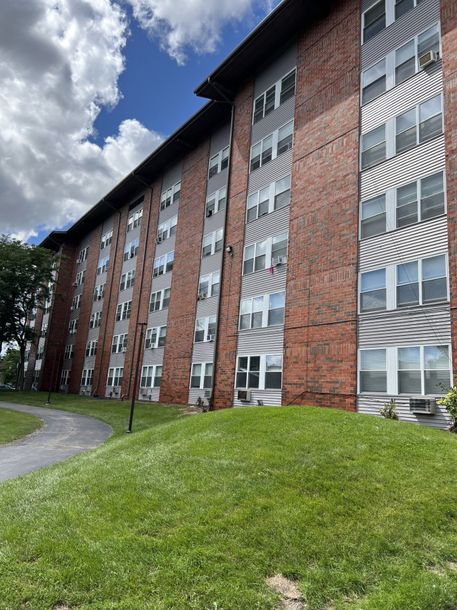 Brick apartment building with white balconies and green lawn under a cloudy sky