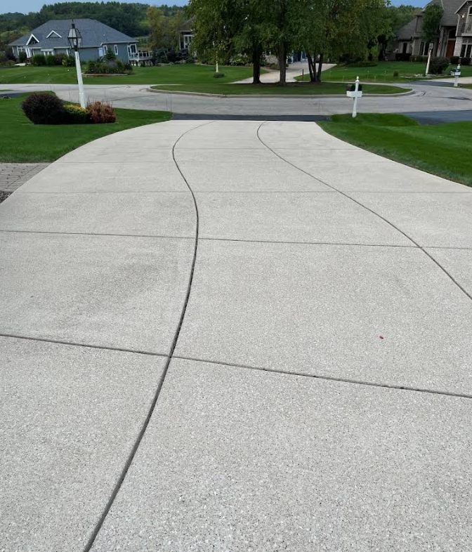 Cracked concrete driveway leading to a quiet suburban street with houses and trees in the background