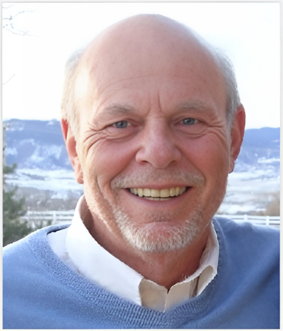 A bald man with a beard wearing a blue sweater smiles for the camera