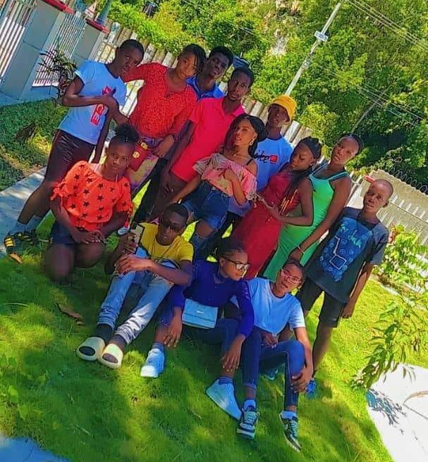Group of teens posing on grass. Bright clothing, sunny outdoor setting.