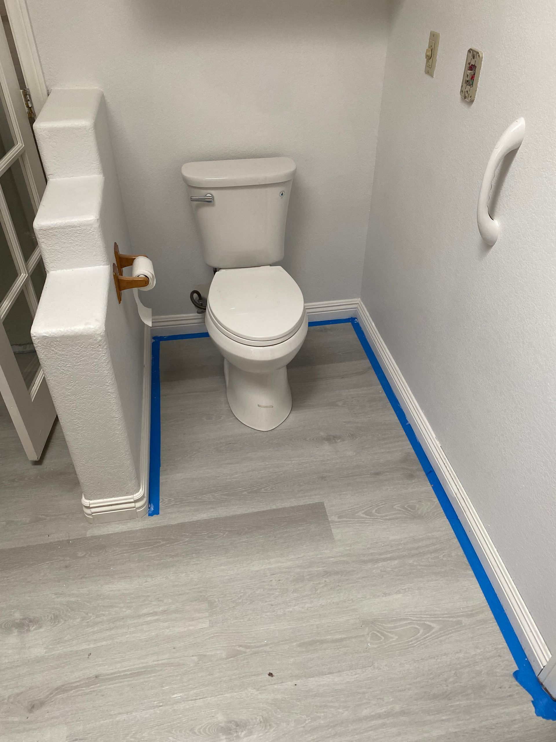 A bathroom with a toilet and a blue tape on the floor.