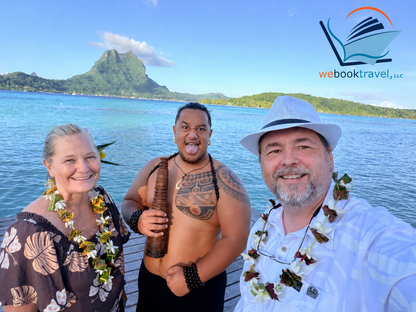 Three people smiling on a sunny beach with blue water and green cliffs in the background