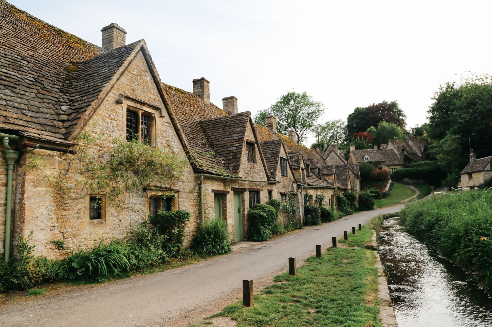 Stone cottages line a road, beside a stream in a village.