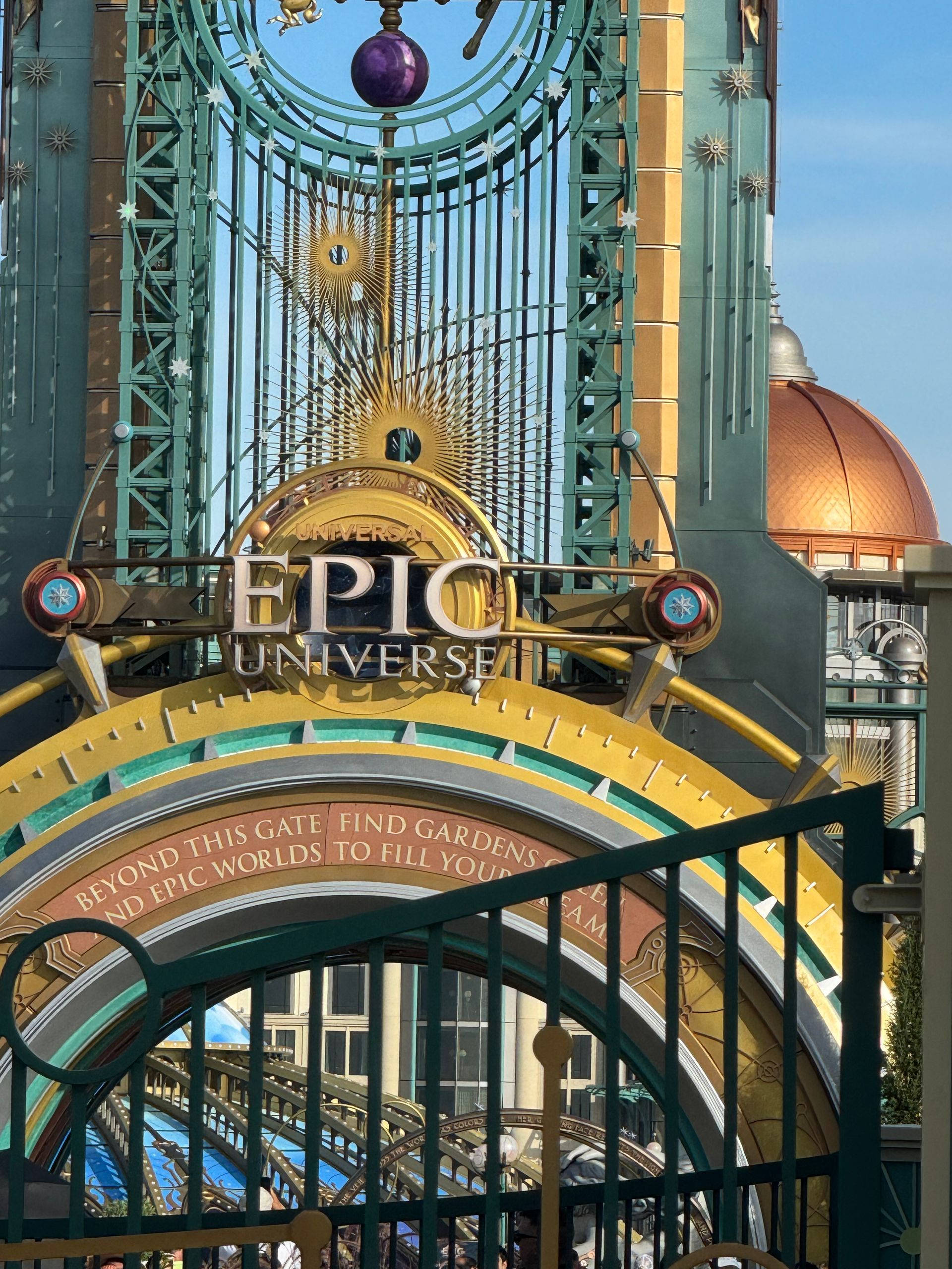 Entrance archway to Epic Universe, gold and teal steampunk design with a bronze dome in the background.