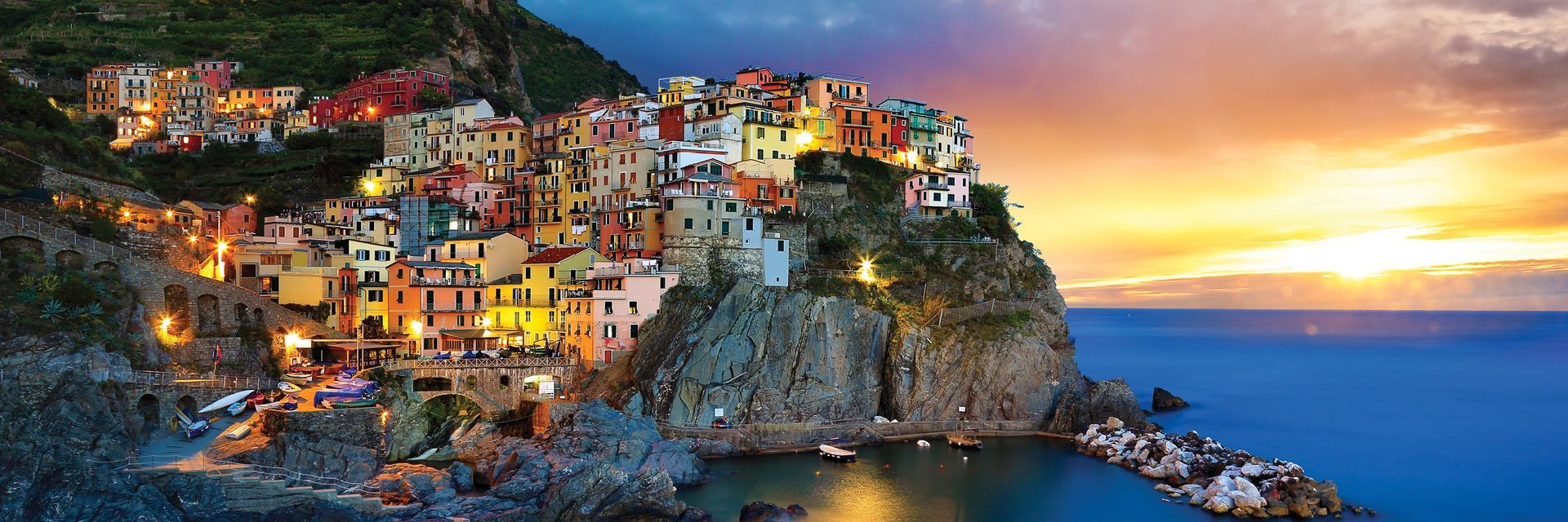 Coastal Italian village at sunset, colorful buildings on a cliff overlooking the sea.