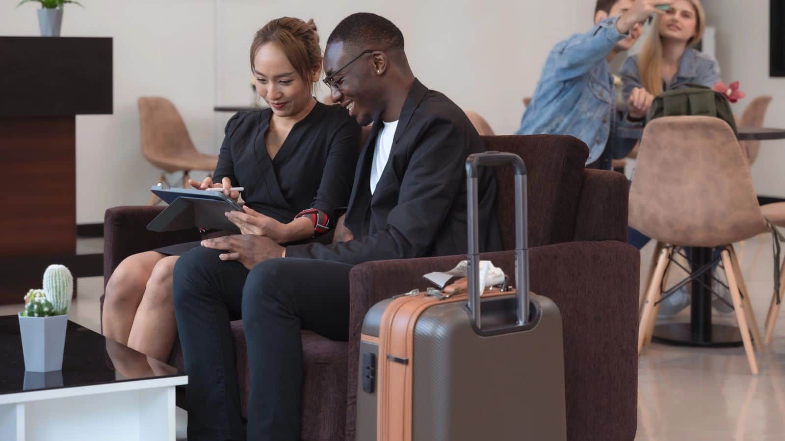 Travelers waiting with luggage beneath airport departure screens