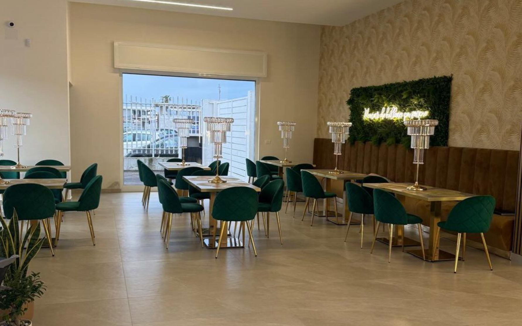 L'interno di un locale caratterizzato da tavoli con sedie in velluto verde, centrotavola in cristallo e un'insegna al neon.