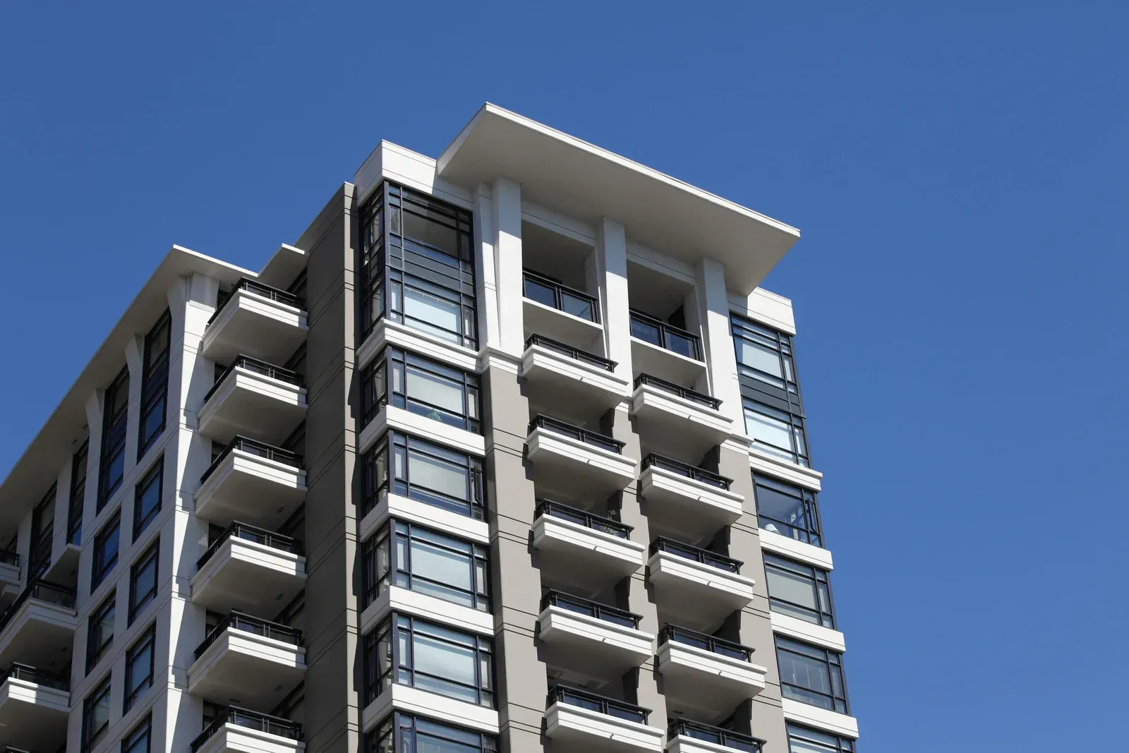 Modern multi-story apartment building with balconies against a clear blue sky.
