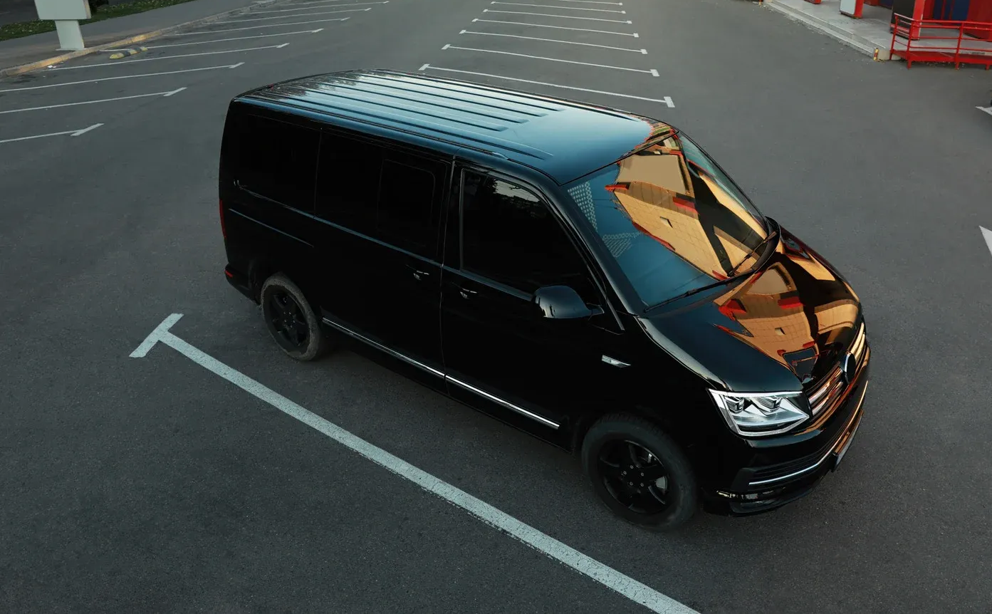Black van parked in an empty parking space, reflecting the surroundings in its windows.