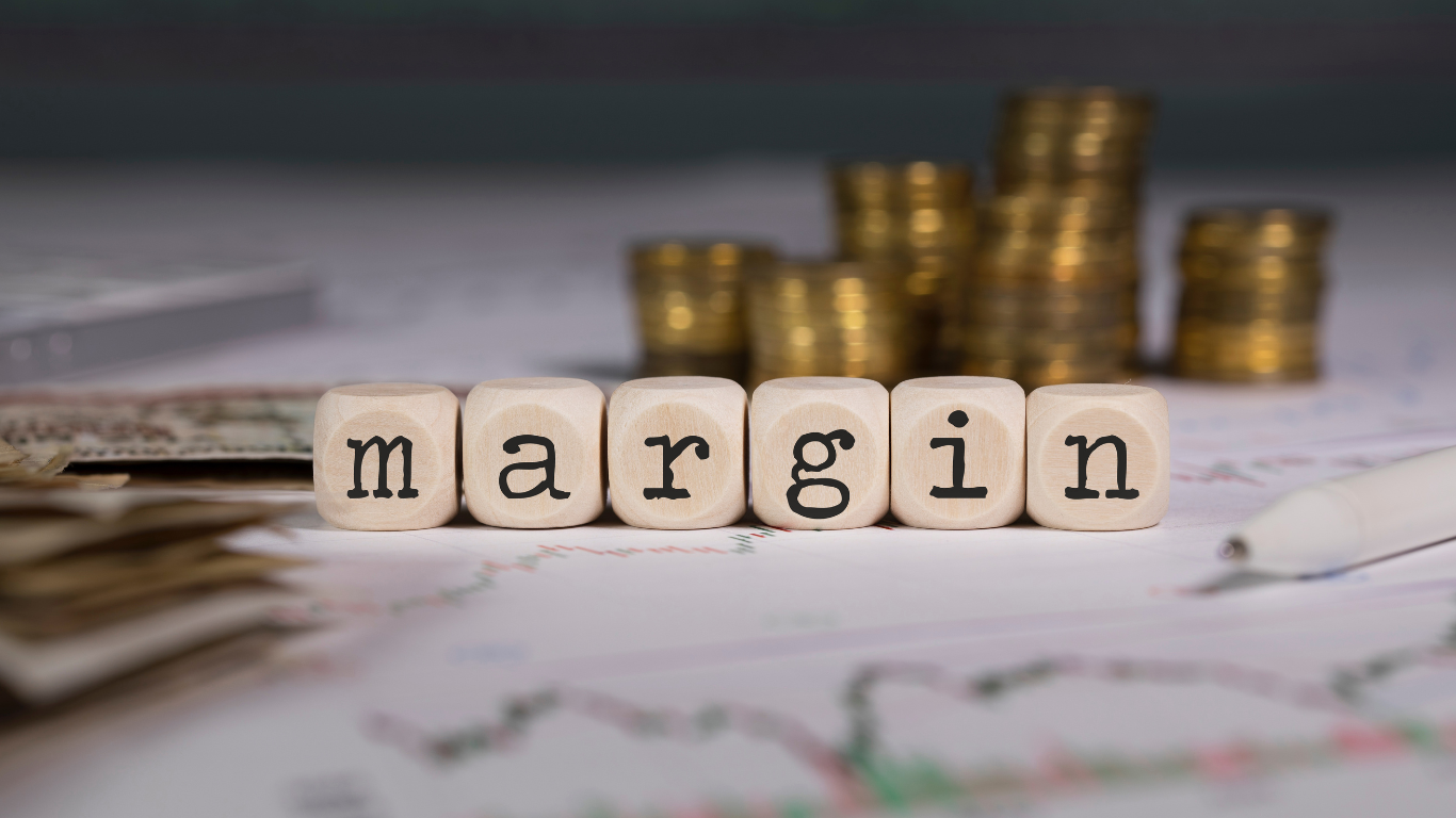 The word margin is written on wooden cubes with coins in the background.