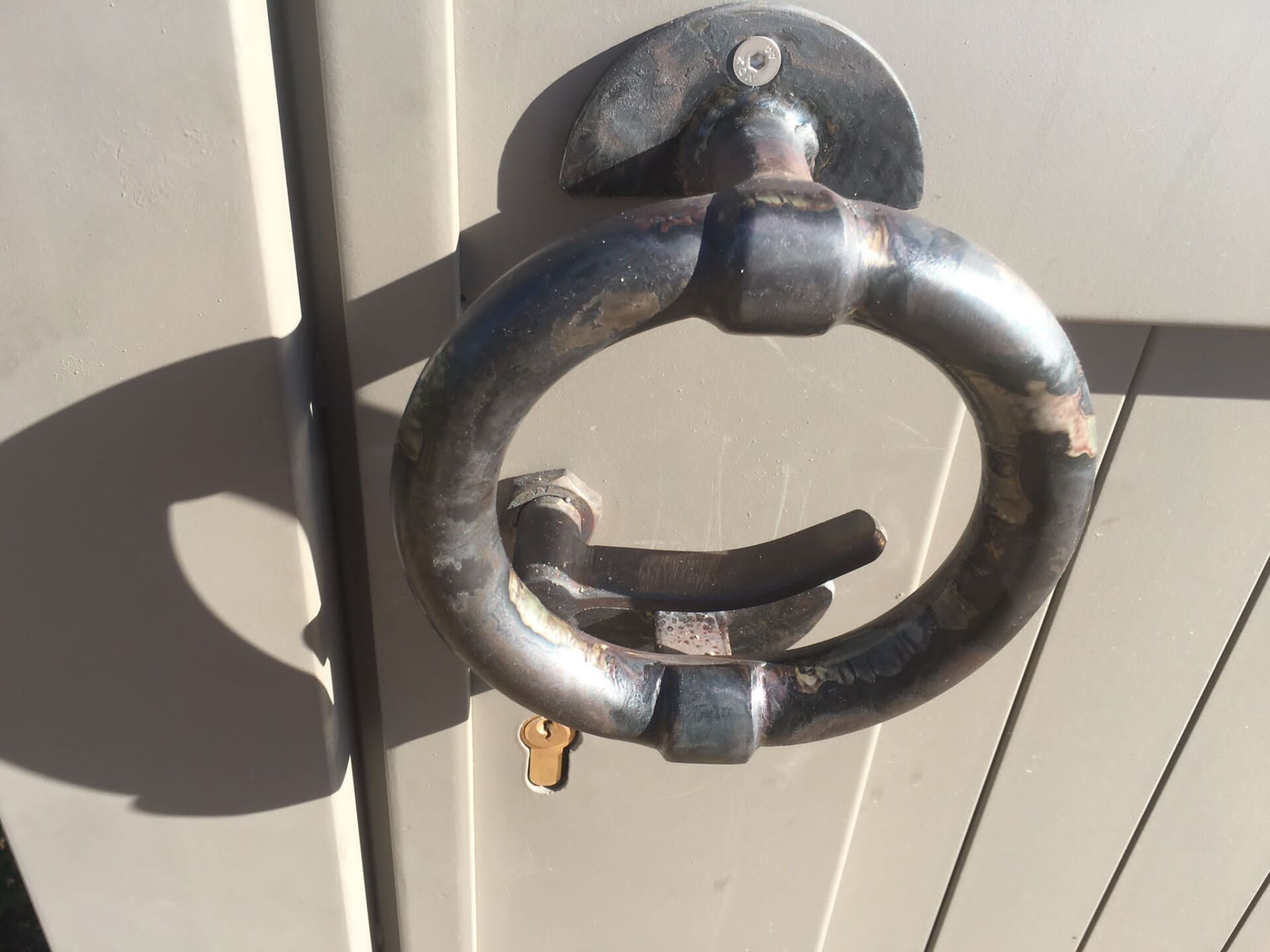 Primo piano di un battente ad anello in metallo nero su una porta chiara, con la luce del sole che proietta un'ombra.
